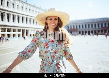 Bonne femme moderne en robe fleurie avec chapeau explorant les attractions de la place Saint-Marc à Venise, Italie. Banque D'Images