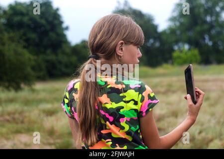 Flou artistique en selfies. Petite fille pose et prend un selfie à la main. Vue arrière de charmante jeune fille en été debout sur la prairie et prendre un selfie sur Banque D'Images