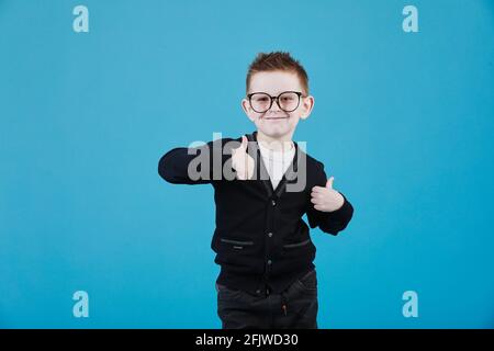 Comme. Portrait d'un petit garçon d'école heureux avec des lunettes souriant à l'appareil photo et faisant le pouce vers le haut geste, montrant l'approbation d'accord cool. Studio d'intérieur s Banque D'Images