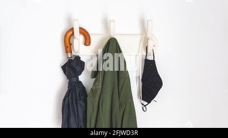 les choses dont vous avez besoin si vous sortez dans la nouvelle normale en raison de covid-19. Pendre d'un porte-manteau un parapluie, un manteau, des masques faciaux et un casque Banque D'Images