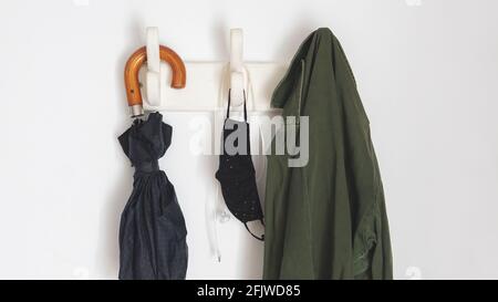 les choses dont vous avez besoin si vous sortez dans la nouvelle normale en raison de covid-19. Pendre d'un porte-manteau un parapluie, un manteau, des masques faciaux et un casque Banque D'Images