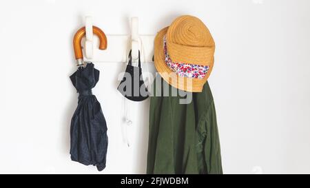les choses dont vous avez besoin si vous sortez dans la nouvelle normale en raison de covid-19. Pendre d'un porte-manteau un parapluie, un manteau, des masques faciaux et un casque Banque D'Images