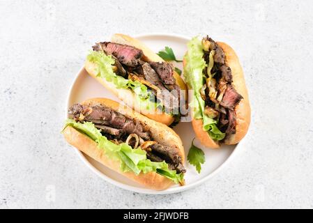 Sandwichs au bœuf avec oignon caramélisé sur plaque sur fond de pierre clair. Vue rapprochée Banque D'Images