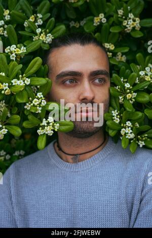 Portrait d'un homme avec sa tête parmi les fleurs. Feuilles vertes et fleurs blanches. Caucasien, avec col et chandail gris. Il a une barbe de quelques jours Banque D'Images