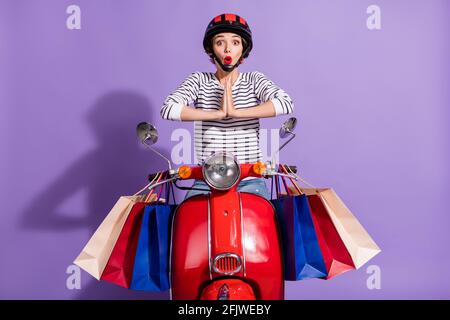 Photo de drôles conducteur femme porter une tenue à rayures casque rouge les bras de vélo assis ensemble demandent à acheter de nouveaux vêtements isolés arrière-plan violet Banque D'Images