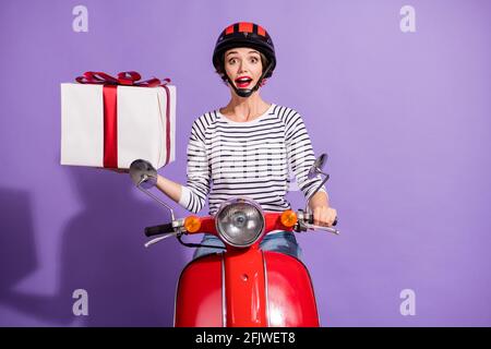 Photo portrait d'une fille surprise sur une moto en regardant un casque maintien de l'isolement de la boîte actuelle sur un arrière-plan violet vif Banque D'Images