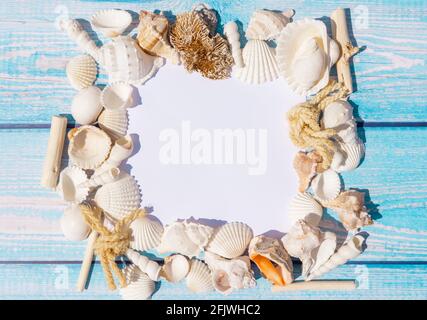 Vue de dessus de la carte en papier blanc pour photo ou lettrage avec coquillages et étoiles de mer sur fond bleu en bois. Concept de vacances d'été. Banque D'Images