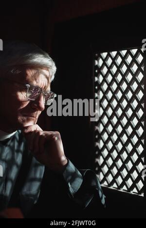 Homme senior dans des lunettes assis derrière la grille et à l'écoute à la personne fidèle Banque D'Images