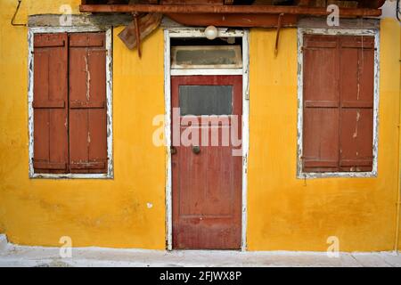 Ancienne façade de maison vénitienne abandonnée avec un mur en stuc ocre et une porte et des volets en bois altérés à Nafplio, Argolis Péloponnèse, Grèce. Banque D'Images