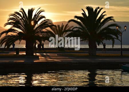 Paysage de coucher de soleil avec palmiers et silhouettes de personnes au Vieux Port de Nafplio à Argolis Péloponnèse, Grèce. Banque D'Images