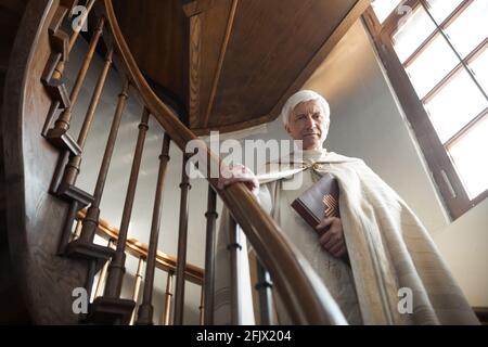 Portrait du prêtre senior tenant la Bible et regardant la caméra en vous tenant sur des escaliers en bois dans l'église Banque D'Images