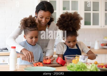 Bonne maman enseignant à deux enfants d'âge préscolaire de préparer un repas végétarien Banque D'Images