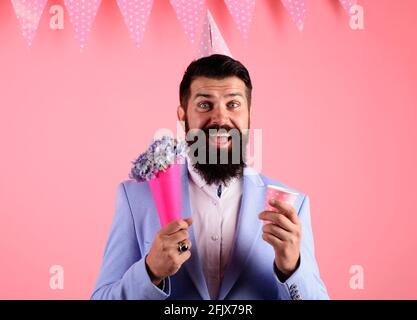 Fête d'anniversaire. Homme barbu souriant dans un chapeau de fête avec bouquet de fleurs. Banque D'Images