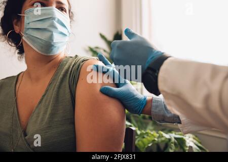 Femme regardant un professionnel de la santé tout en faisant une injection de vaccin sur son bras. Femme dans le masque facial se faire vacciner contre le covid à la maison. Banque D'Images