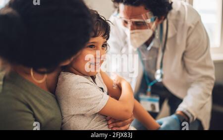 Un garçon heureux avec une maman qui reçoit un vaccin d'un médecin à la maison. Enfant souriant tout en recevant le vaccin Covid à la maison. Banque D'Images