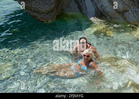 Deux femmes posent dans l'eau de mer transparente sur les pierres légères d'une plage côtière peu profonde de Lucice près de Petrovac, au Monténégro. Banque D'Images
