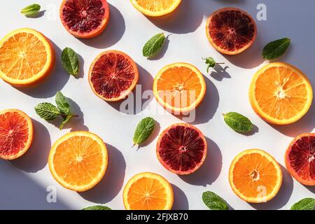 Différentes tranches d'agrumes oranges rouges et oranges vertes feuilles de menthe sur fond blanc avec ombres Banque D'Images
