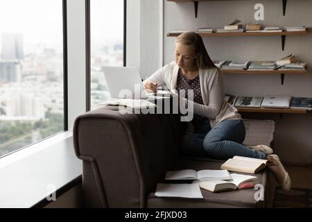 Étudiante du millénaire occupée à étudier en ligne avec des livres Banque D'Images
