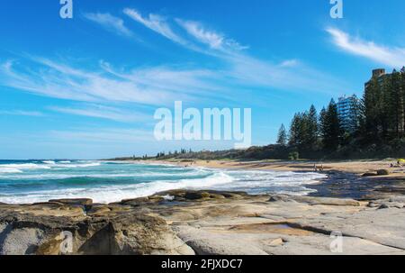 Plage de la Sunshine Coast australienne avec roche volcanique en premier plan et les gens et les chiens appréciant la journée ensoleillée Banque D'Images