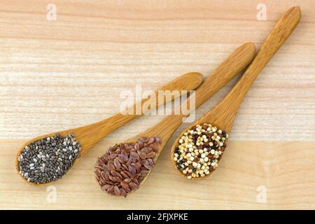 Graines de Chia séchées, graines de lin, graines de quinoa mélange de trois couleurs sur une cuillère en bois, fond de bois Banque D'Images