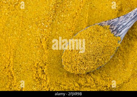 Vue de dessus de la poudre de curry jaune épicée dans une cuillère en bois, assaisonnement des ingrédients principaux pour cuire le curry asiatique sur fond d'épices flou Banque D'Images