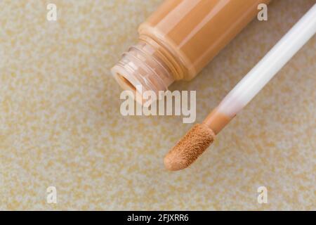 Applicateur pour pied de biche à côté du tube de correcteur crémeux, couverture haute pour dissimuler les taches, les imperfections, sur fond de carreaux jaunes Banque D'Images