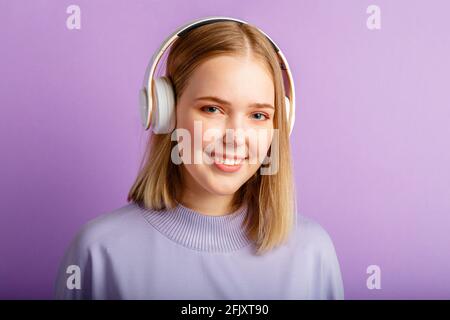 Bonne jeune femme dans le portrait de casque. Belle femme souriante avec une coiffure blonde Profitez de la musique de chanson dans un casque isolé au-dessus de violet Banque D'Images