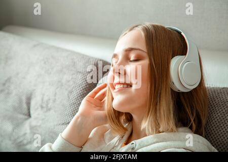 Bonne jeune femme assise sur un canapé dans un casque. Femme ou jeune fille se reposant, Bliss profiter d'écouter de la musique sur le canapé à l'intérieur de la maison de la salle de séjour Banque D'Images