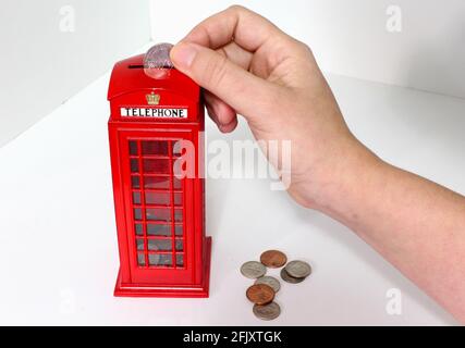 La main de la femme dépose des pièces dans une banque de pièces de London Phone Booth. Kiosque téléphonique rouge britannique. Tirelire. Banque D'Images