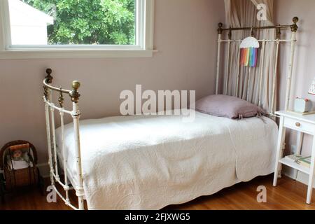 Chambre des filles. Lit à baldaquin avec cadre en fer et petite lampe de bureau sur une table de nuit. Un petit chariot de bébé est dans la chambre pour jouer. Grande fenêtre d'espace ouvert Banque D'Images