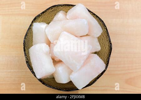 Pangasius surgelé, poisson de Cory coupé en cube dans un bol en verre, vue du dessus. Filet de poisson d'eau douce en morceaux, sur fond de bois Banque D'Images