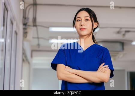 Portrait d'une jeune et belle infirmière confiante portant un uniforme debout avec les bras croisés dans l'hôpital regardant la caméra avec fierté au service des patients infectés par le covid-19 Banque D'Images