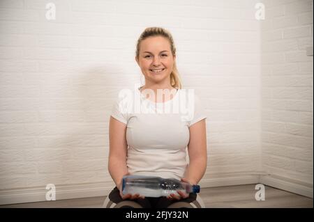 Bonne femme blonde faisant de l'exercice de forme physique avec des bouteilles d'eau - entraînement sportif de base comme entraînement à la maison Banque D'Images