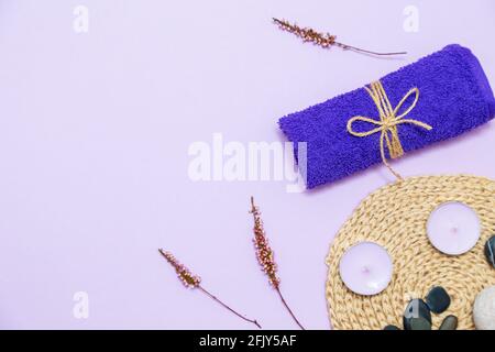 Bougies parfumées, serviette, lotion et cailloux sur fond lilas. Vue de dessus, espace de copie, plan de travail. Concept spa et soins du corps. Banque D'Images