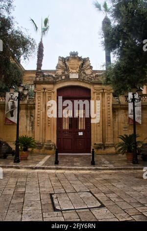 Porte voûtée avec des portes rouges à côté de la rue le jour des pluies à Mdina, Malte. Banque D'Images