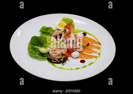 cocktail de crevettes et salade gravlax de saumon mariné avec petit bijou laitue et herbes dans une assiette blanche avec fond noir Banque D'Images