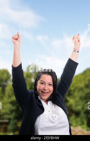 Femme d'affaires gaie portant un costume chic et décontracté pour célébrer ses gestes avec fists et happy expression comme concept d'entreprise sur la nature du parc arrière-plan Banque D'Images