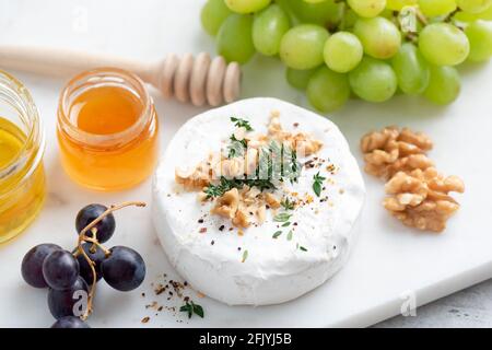 Camembert entier ou brie sur un plateau de fromages servi avec du raisin, du miel, des noix et du thym Banque D'Images