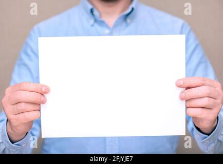 Un homme en chemise bleue, homme d'affaires tenant une feuille blanche. Espace pour le texte, maquette Banque D'Images