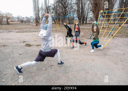 Cours de fitness en groupe à l'extérieur. Cours d'entraînement en plein air socialement distants dans les parcs publics. Trois femmes et l'homme s'entraîner ensemble dans le public Banque D'Images