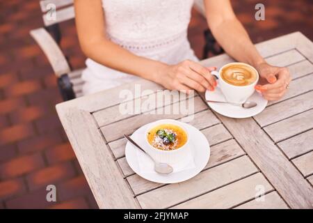 une femme boit une délicieuse caféine boire un latte aromatique avec un dessert français de crème anglaise recouverte de sucre caramélisé Banque D'Images
