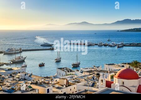 Belle vue sur Chora, Mykonos, Grèce au coucher du soleil. Port, baie, bateaux, yachts amarrés par la jetée. Célèbres maisons blanchies à la chaux, église blanche avec dôme rouge Banque D'Images