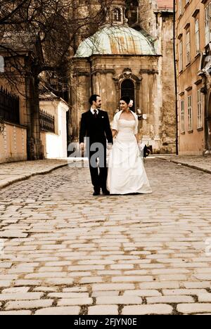 Magnifique couple de mariage (mariée et marié) marchant dans la rue en face de l'église historique et regardant l'un l'autre. Banque D'Images