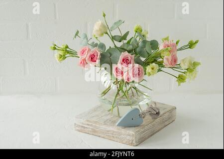 Bouquet de roses, d'euphorie et d'eucalyptus dans un vase en verre élégant sur une table. Composition des fleurs pour la décoration intérieure Banque D'Images