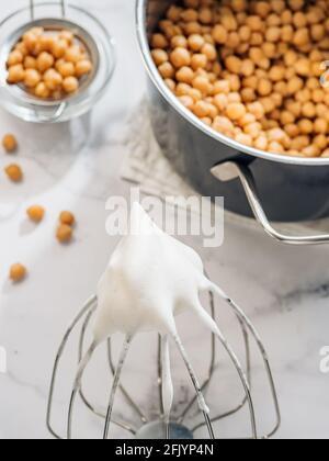 Fouettée aquafaba sur fouet planétaire, vertical. Eau de pois chiches saumure aquafaba fouettée. Remplacement de l'œuf en cococokéfaction. Concept vegan. Vue de dessus ou plan de travail Banque D'Images