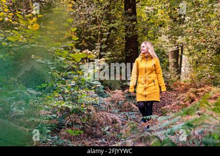 Femme blonde en blouson jaune marchant dans une forêt défrichant surcultivé avec de la fougère Banque D'Images