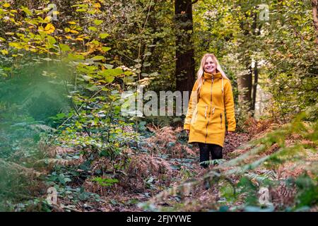 Femme blonde en blouson jaune marchant dans une forêt défrichant surcultivé avec de la fougère Banque D'Images