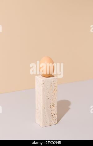 Œuf simple debout sur un bloc de marbre travertin sur fond beige et gris. 2021 composition unique de la vie surréaliste de Pâques. Banque D'Images