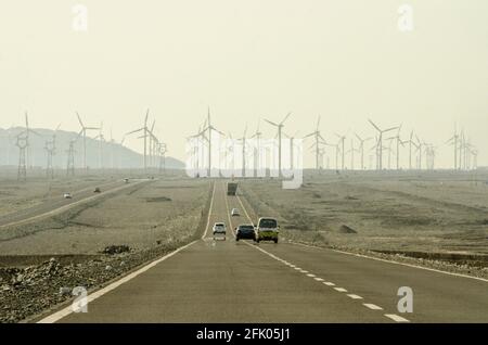 Les voitures roulent le long de l'autoroute G312 dans une brume de chaleur scintillante, passant par des éoliennes et des lignes électriques qui sillonnent le désert à la périphérie ouest de Turpan, dans l'un des endroits les plus chauds de la planète. Les énergies renouvelables éoliennes sont de plus en plus utilisées par les Chinois pour développer leurs industries gourmandes en énergie, comme on le voit ici dans le Xinjiang oriental, en Chine, en RPC. © Time-snapshots Banque D'Images