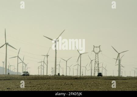 Les voitures roulent le long de l'autoroute G312 dans une brume de chaleur scintillante, passant par des éoliennes et des lignes électriques qui sillonnent le désert à la périphérie ouest de Turpan, dans l'un des endroits les plus chauds de la planète. Les énergies renouvelables éoliennes sont de plus en plus utilisées par les Chinois pour développer leurs industries gourmandes en énergie, comme on le voit ici dans le Xinjiang oriental, en Chine, en RPC. © Time-snapshots Banque D'Images